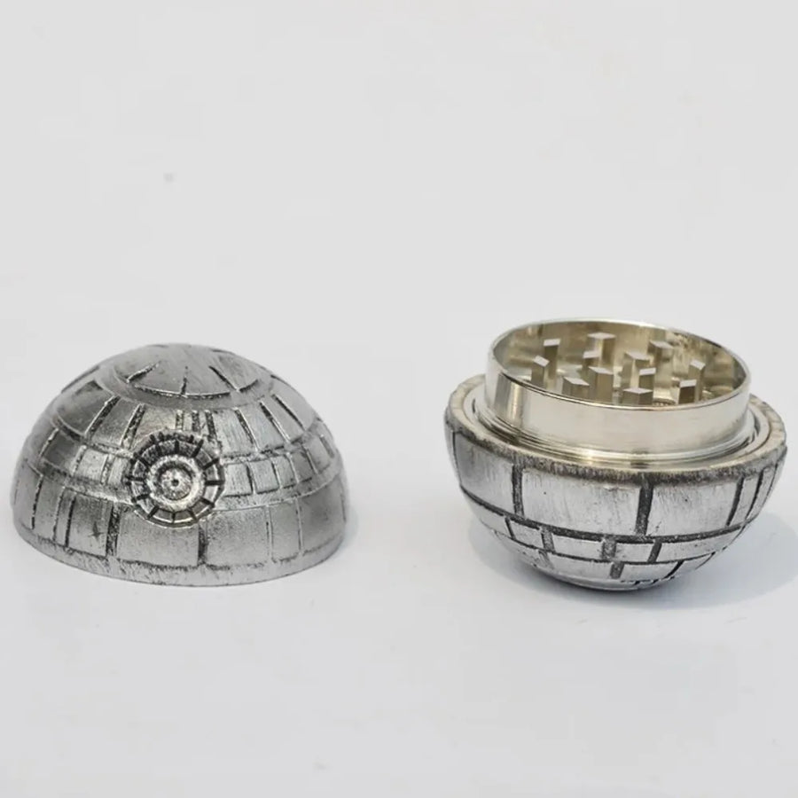 A silver-toned metal herb grinder shaped like the Death Star, shown disassembled with the dome lid on the left and the lower half with grinding teeth on the right, set against a plain white background.